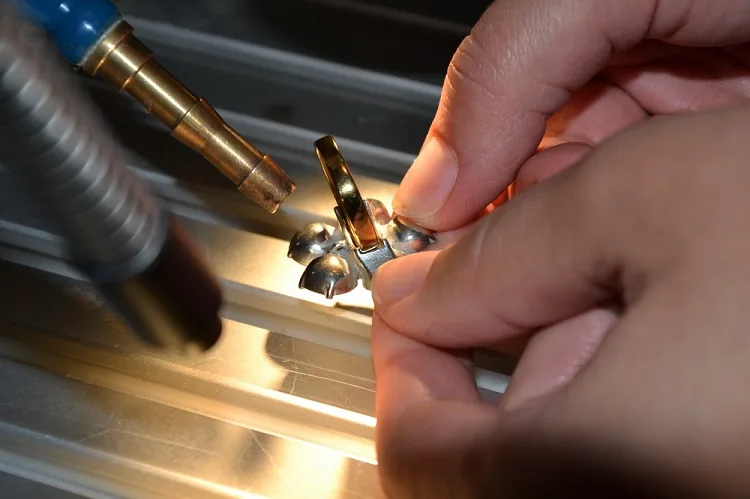 Zwei Hände führen ein kleines Goldteil unter dem Laserschweißkopf
